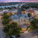 Aerial view of the historic Hood County Courthouse and downtown Granbury square at dusk, with Lake Granbury in the background